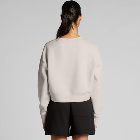 A light grey crop crew jumper viewed from the back, paired with black shorts. The design features a simple silhouette and a logo.