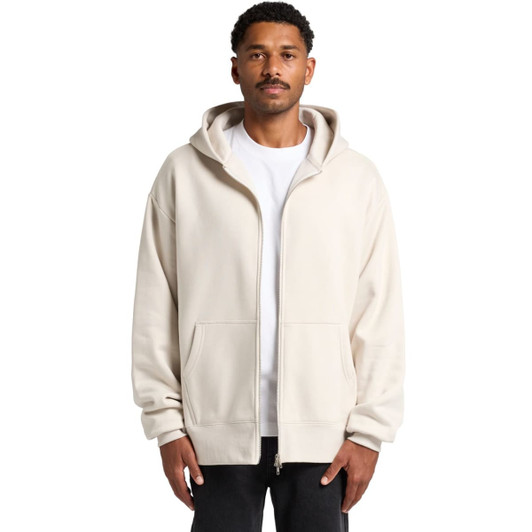 A man wearing a cream heavy zip hoodie with a front pocket and a hood, featuring a logo.