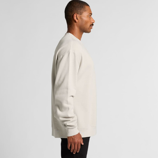 A side view of a relaxed-fit, faded crew jumper in a light beige colour. The garment features long sleeves and a logo.