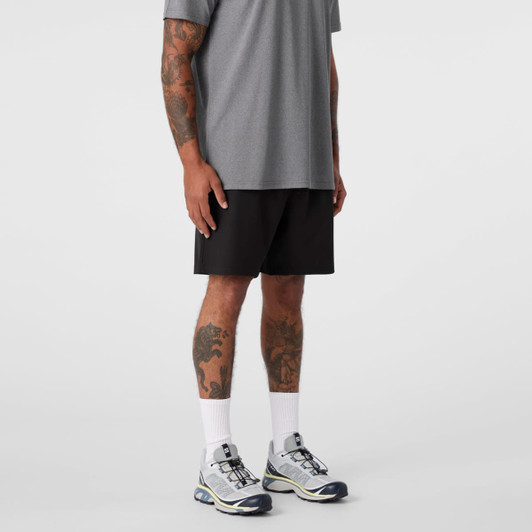 A man stands wearing grey sports shorts and a matching grey top, paired with white socks and grey shoes.