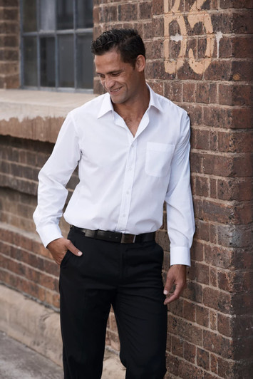 A long sleeve white button-up shirt on a man, paired with black trousers, against a brick wall background.