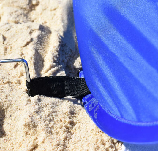A blue pop-up beach shelter with a black anchoring strap partially buried in the sand.