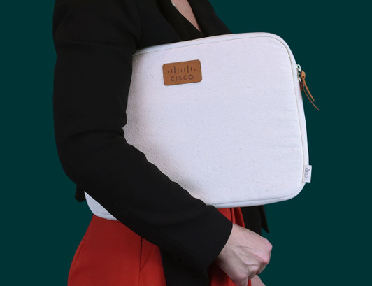 A cream laptop sleeve with a leather tag, being held by a person in a black jacket.