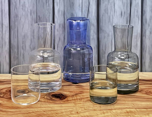 A glassware set featuring a blue carafe and four tumblers in clear and tinted glass on a wooden surface.