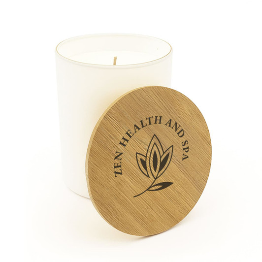 A large white glass candle with a wooden lid featuring a logo and a simple leaf design.