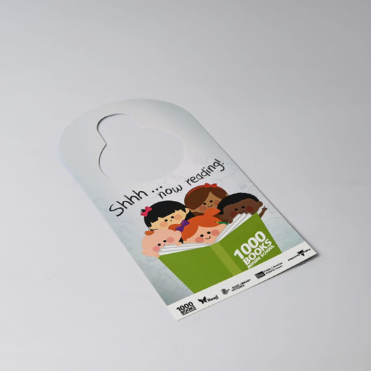 A double-sided door hanger featuring illustrations of children reading and a circular cut-out at the top.