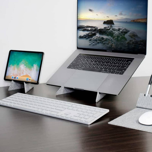A grey eco laptop stand displaying a laptop and tablet, alongside a sleek keyboard and mouse on a matching mat.