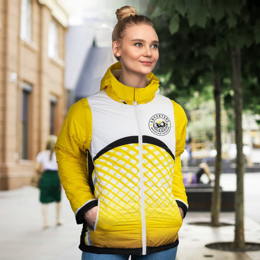 A woman is wearing a custom reversible puffer jacket in yellow and white, featuring a logo and a modern design.