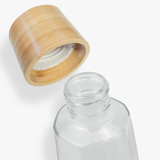 A glass drink bottle with a bamboo lid. The bottle has an octagonal shape and is transparent.