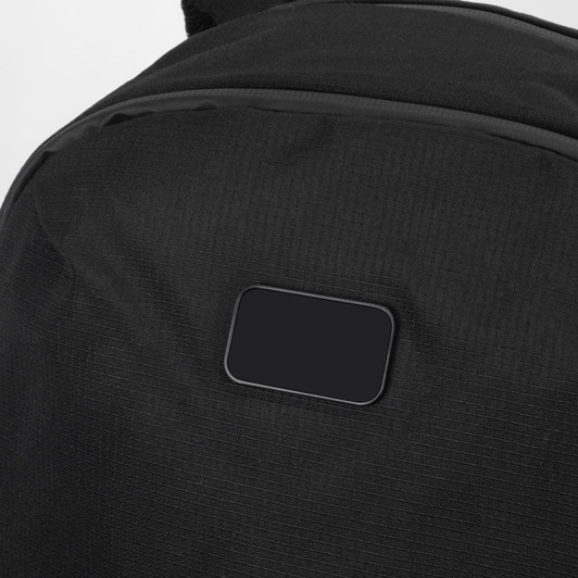 A black backpack with a textured surface and a small, blank rectangular area. It features a logo or branding.