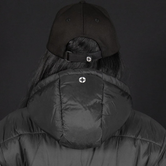 A black puffer jacket with a hood, worn by a person wearing a black cap, featuring a logo on the back.