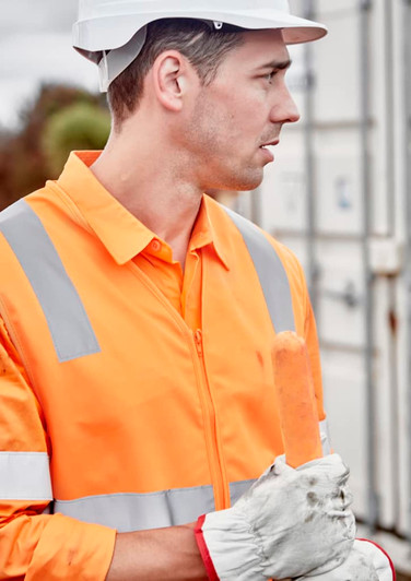 A man wearing an orange hi-vis zip vest with reflective strips and a white hard hat, holding a sausage.