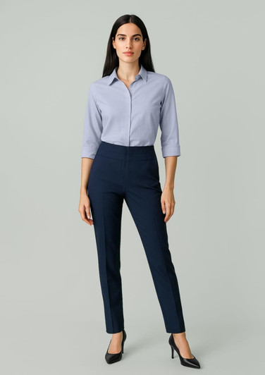 A woman modeling navy slim leg pants with a mid-waist design, paired with a light blue shirt. The image includes branding.
