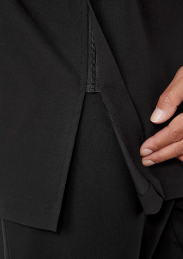 A close-up of a black jacket featuring a zippered slit and a hand holding the fabric. It has a logo.
