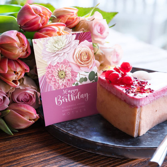 A6 greeting card in pink and floral design beside a cake and a bouquet of pink roses and tulips.