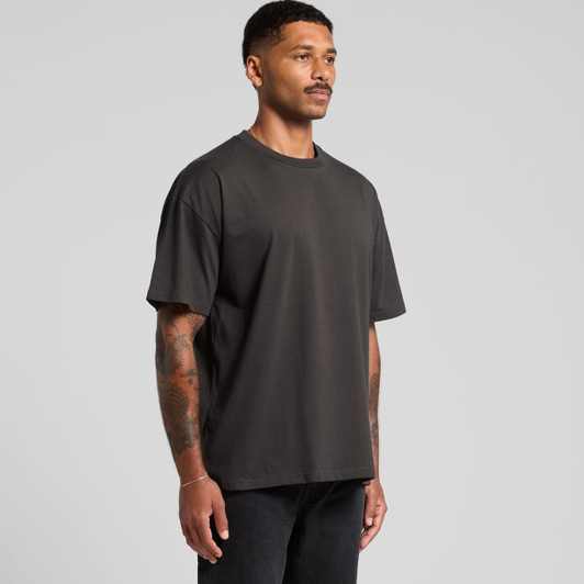 A man wearing a classic oversized tee in dark grey, featuring a logo on the front.