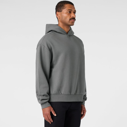 A grey hooded jumper with a relaxed fit, featuring a logo on the front. The model is standing sideways.