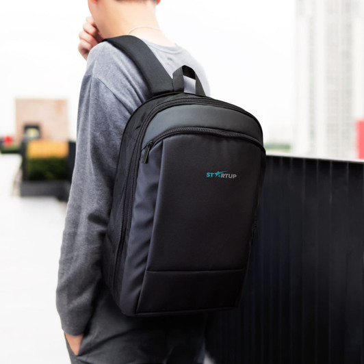 A black Kaden Soft Touch Backpack, carried by a person, featuring a logo and a sleek design.