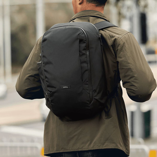 A backpack in black being worn by a person, showcasing a sleek design with a prominent logo on the back.