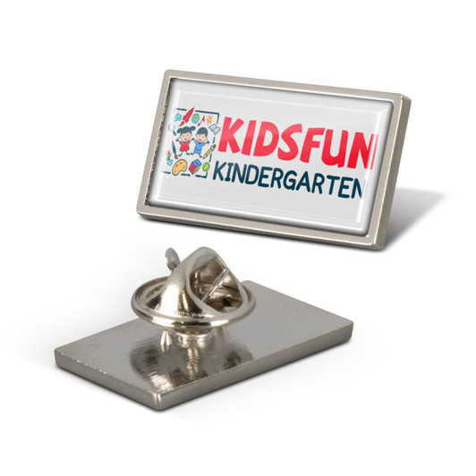 A rectangular lapel pin featuring a colourful design and a silver backing. It includes a logo and a clasp.