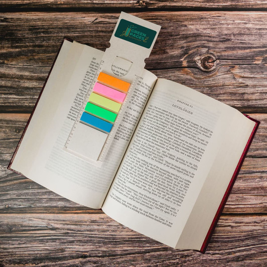 A rectangular bookmark in pastel colours rests in an opened book, featuring a logo at the top.
