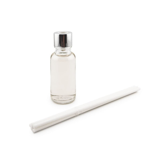 A clear glass bottle with a silver cap and a white reed stick beside it.