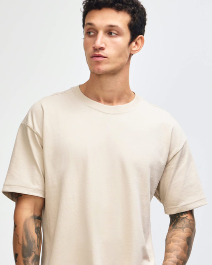 A light beige super heavyweight T-shirt on a model, featuring a relaxed fit and short sleeves. It has a logo.