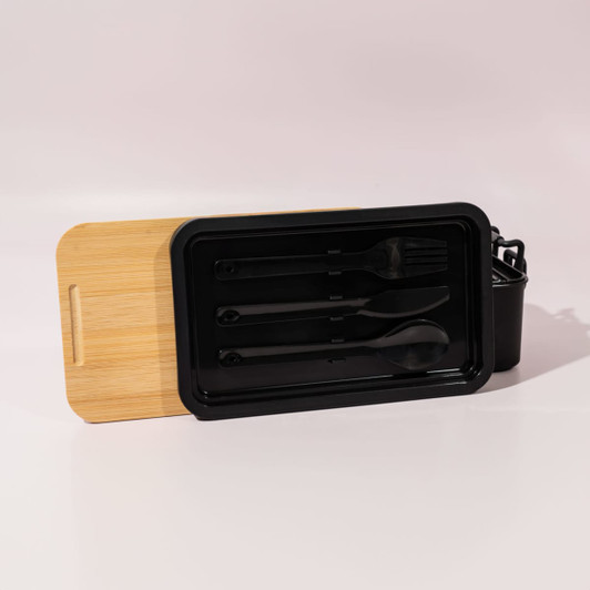 A black lunch box with a bamboo lid and cutlery inside, featuring a fork and spoon. It also has a branding logo.