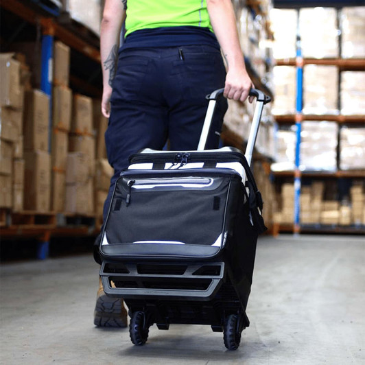 A black rolling cooler with a handle and wheels being pulled in a storage area, featuring a logo.