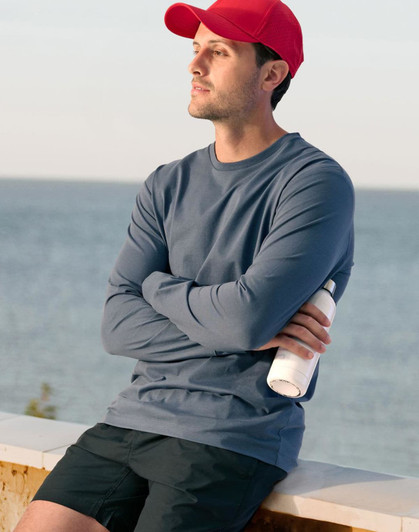 A long-sleeved men's tee shirt in blue, paired with black shorts and a red cap, held with a drink bottle.