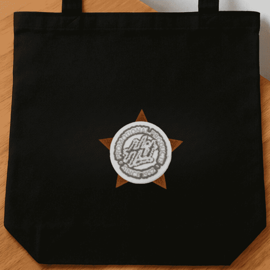 A black tote bag featuring a circular logo set within a star design.
