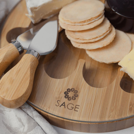 A bamboo cheese board featuring round crackers, cheese, and serving tools. Includes a logo on the board.