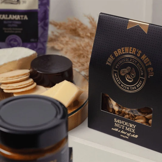 A black packaging of Savoury Nut Mix displayed with various gourmet snacks, including cheese and biscuits.