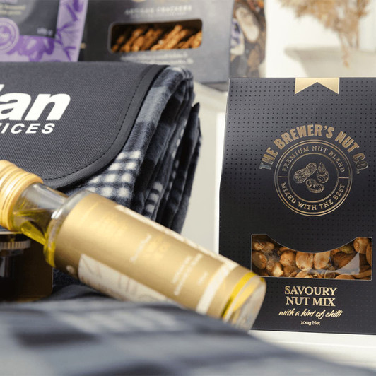 A drink bottle, a picnic blanket, and a Savoury Nut Mix packaged in a black box. The blanket features a checkered pattern.