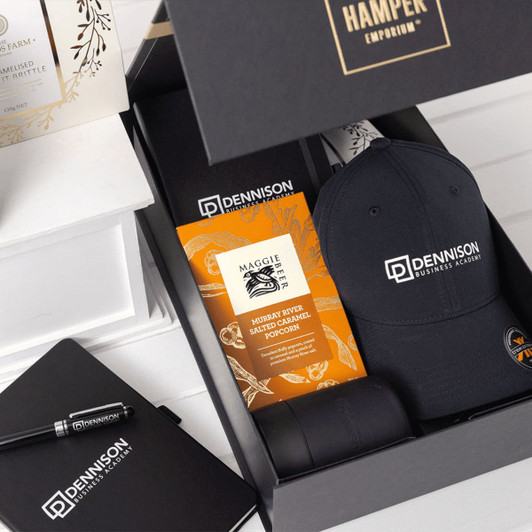 A black cap, a pen, and gourmet popcorn in an elegantly designed gift box featuring a logo.