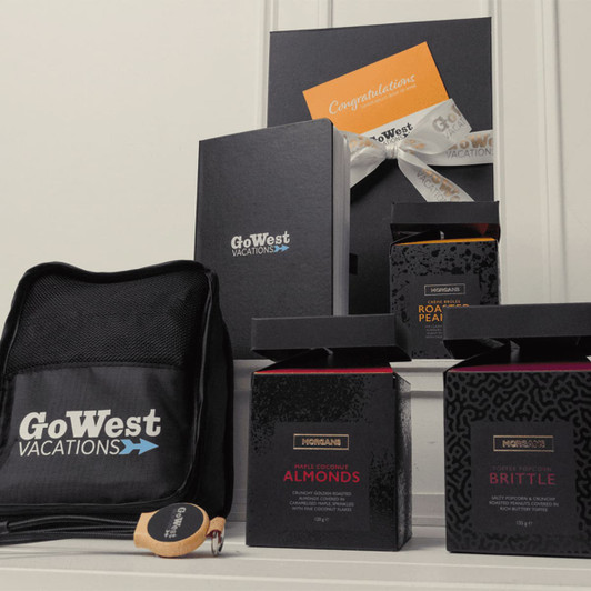 A black bag with a logo, three gift boxes containing snacks, and an orange card with a ribbon.