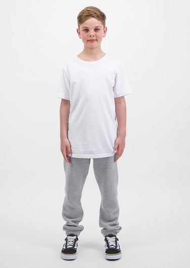 A child stands upright, wearing a plain white t-shirt and grey track pants, with black and white sneakers.