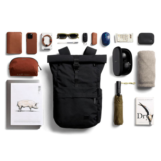 A black rolltop backpack surrounded by various items including sunglasses, a water bottle, tech accessories, and a book.