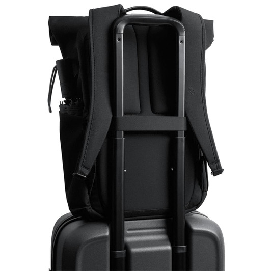 A black rolltop backpack is secured on a black suitcase, featuring padded straps and a side pocket.