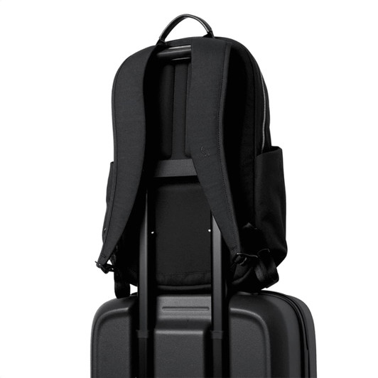 A black backpack rests on top of a black suitcase, with adjustable straps and side pockets visible.