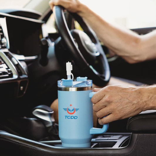 A drink bottle in light blue, featuring a handle and a straw, positioned in a car's centre console.