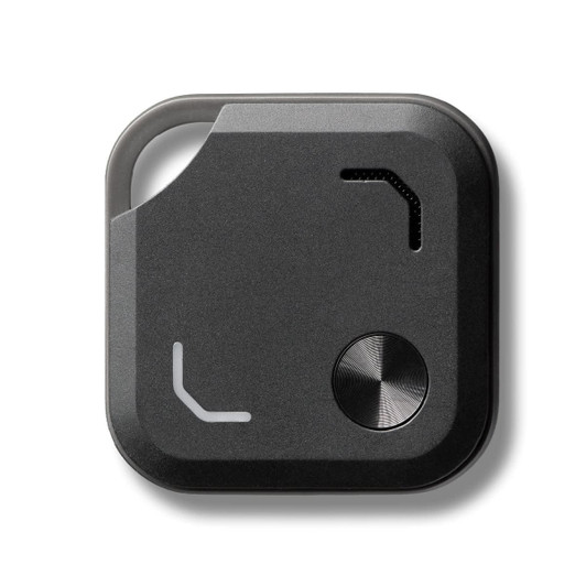 A black Bluetooth tracker featuring a metal button and a small opening, with a minimalist design.