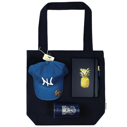 A navy tote bag holds a blue cap, a pineapple notebook, a pen, and a drink bottle, all featuring a logo.