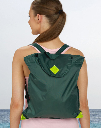 A green excursion bag with a flap and straps worn on the back of a person, set against a beach backdrop.