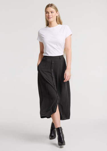 A woman wearing a black maxi skirt paired with a white T-shirt and black ankle boots, featuring a front slit and pockets.