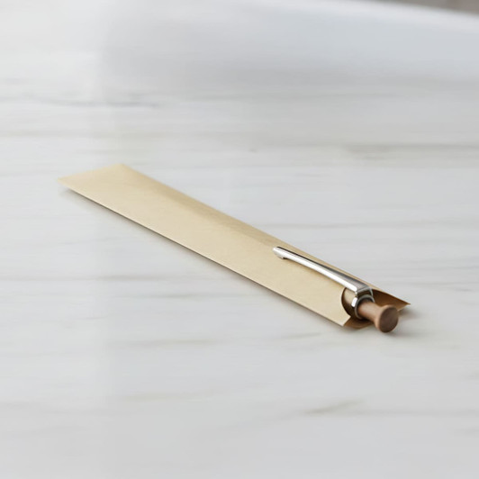 A Kraft paper pen sleeve in a beige shade, containing a silver pen with a wooden barrel, resting on a marble surface.