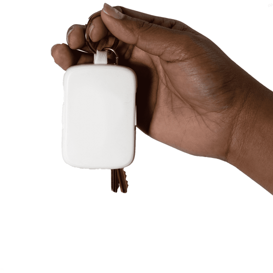 A hand holding a white rectangular powerbank keychain with keyring attachments. The product features a logo.