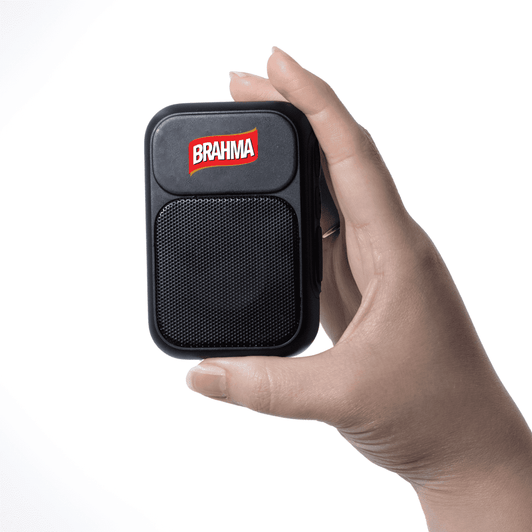 A hand holding a small black speaker with a mesh front and a logo on top.