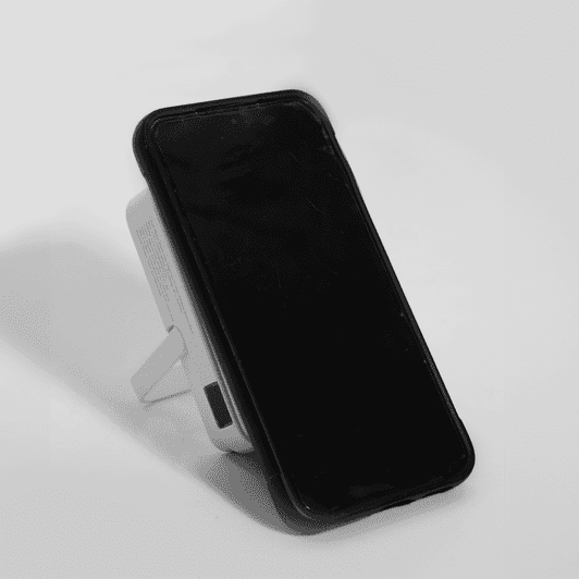 A wireless charging power bank in white, featuring a stand and a black face. It has a logo on the side.