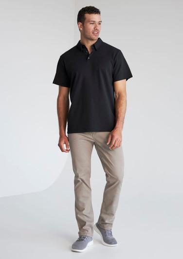 A man wearing a black short sleeve polo shirt and light grey trousers, featuring a logo on the polo.